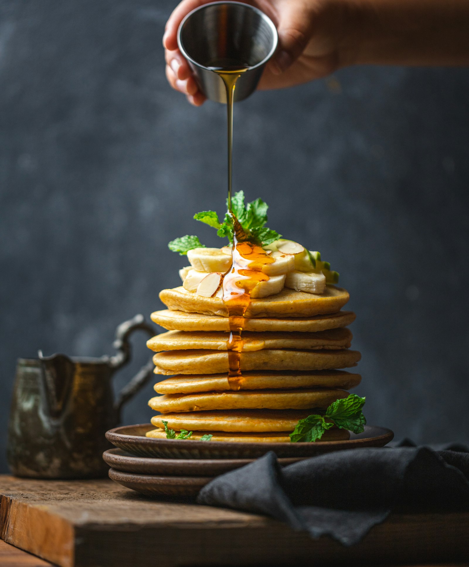 A tall stack of golden pancakes with syrup being poured over them